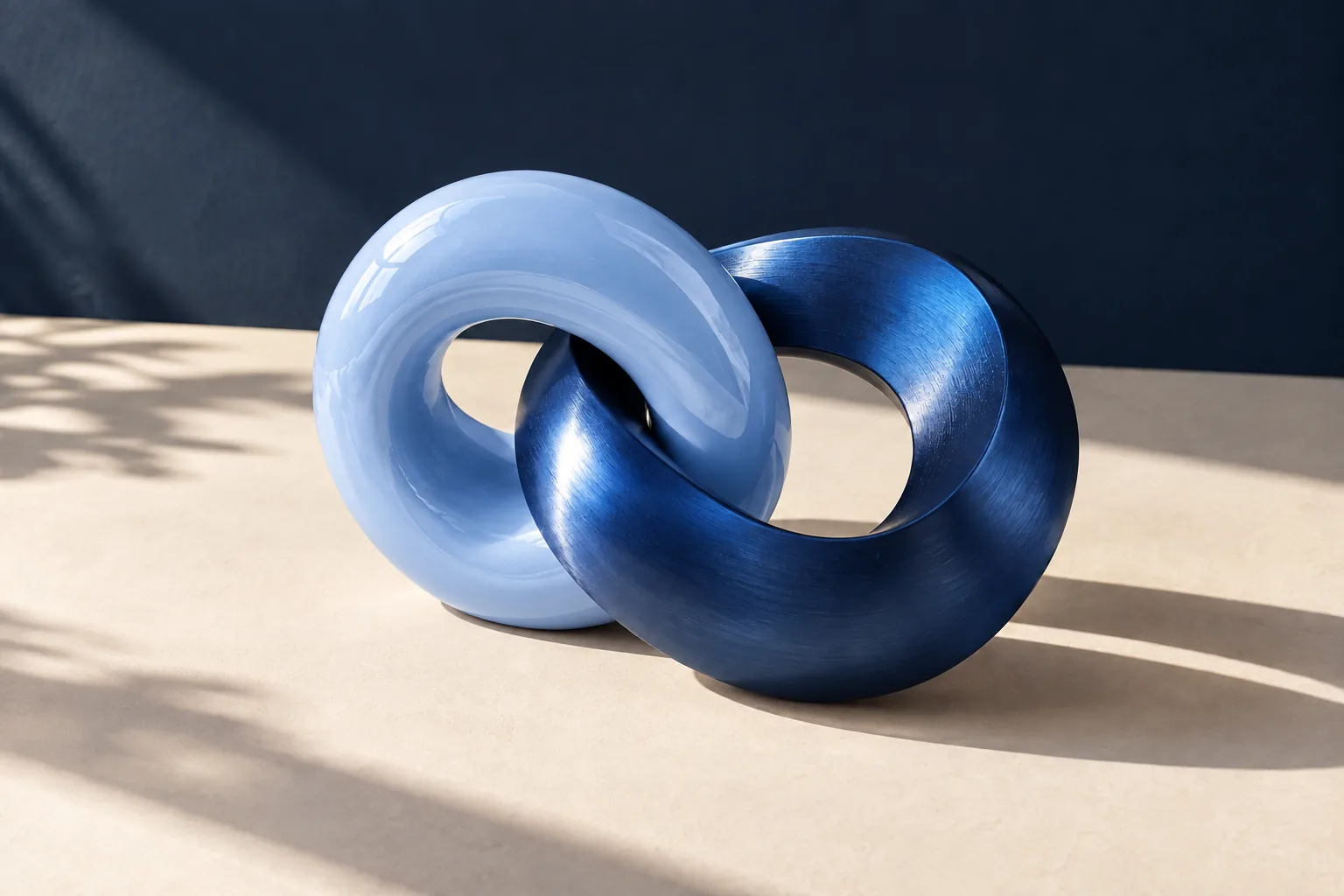 Dos formas entrelazadas de cerámica azul claro y metal cobalto sobre una superficie marfil.